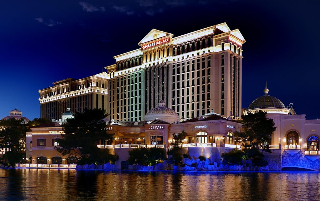 Caesars Palace Las Vegas at night with lit fountain, domed restaurants, and reflections on water.