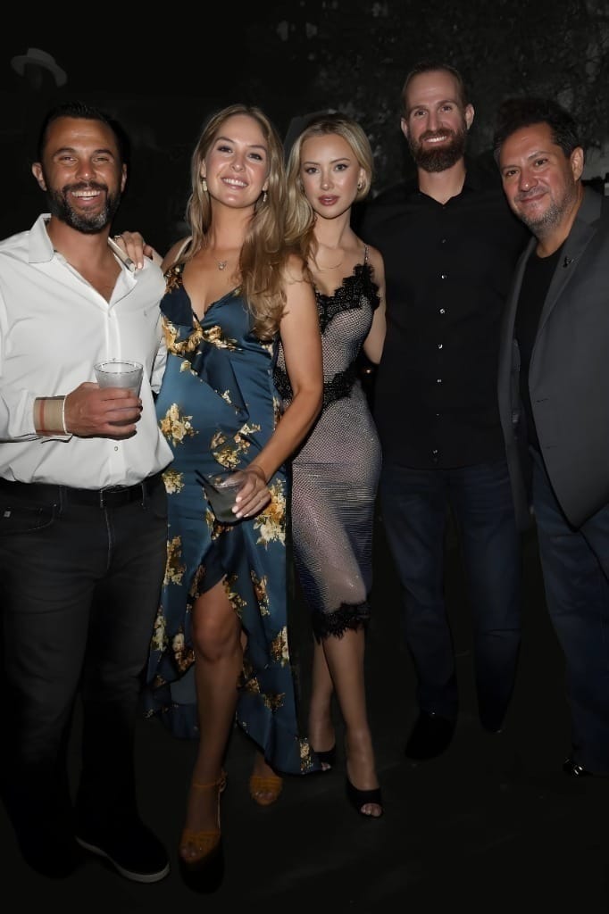 Five adults—three men and two women—smiling and standing close together in a dimly lit indoor setting during a Rogue Bunnies event, dressed in stylish, semi-formal attire.