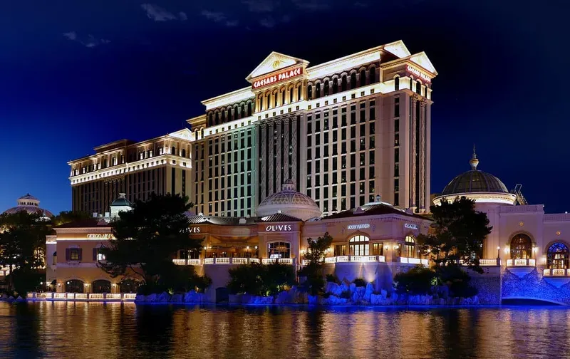 Caesars Palace Las Vegas at night with lit fountain, domed restaurants, and reflections on water.
