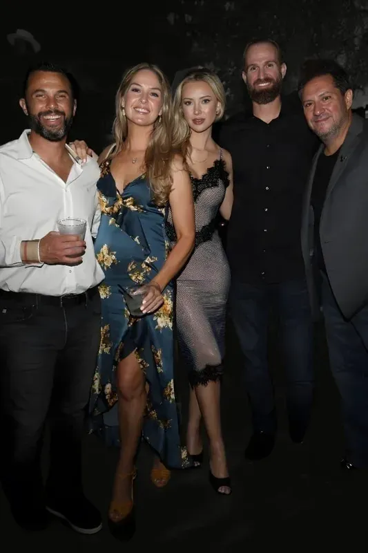 Five adults—three men and two women—smiling and standing close together in a dimly lit indoor setting during a Rogue Bunnies event, dressed in stylish, semi-formal attire.
